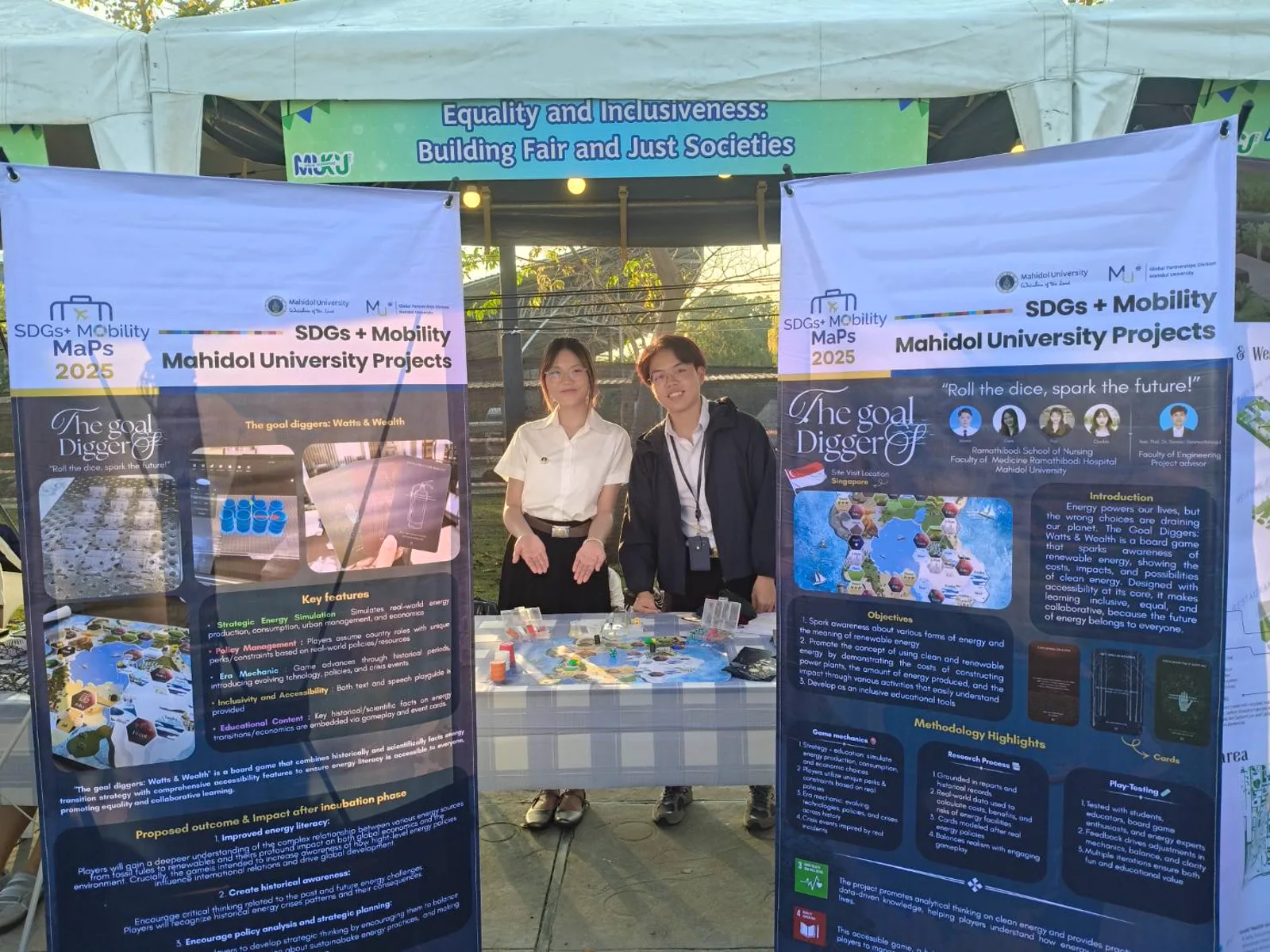 Two team members presenting Watts and Wealth at the SDGs + Mobility MaPs 2025 showcase booth, flanked by two project banners